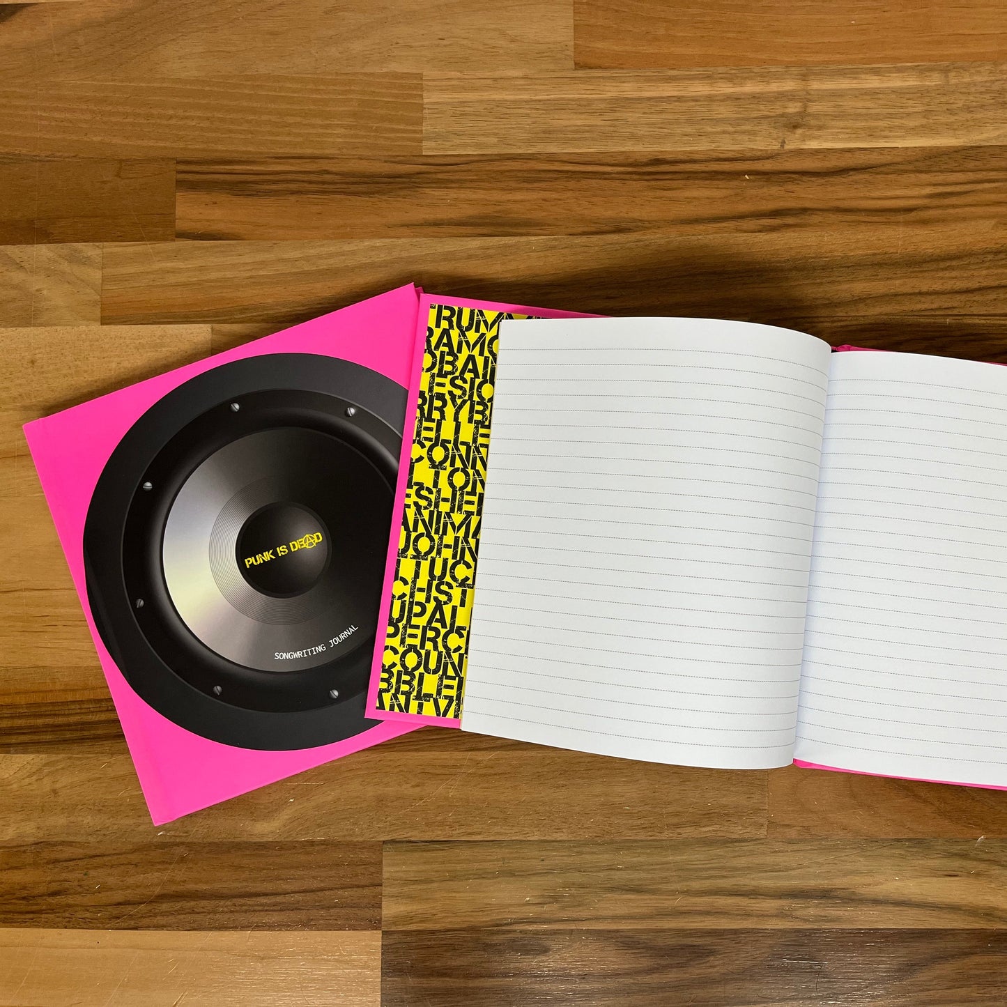 Open notebook with a pink and black speaker on top, on a wooden surface