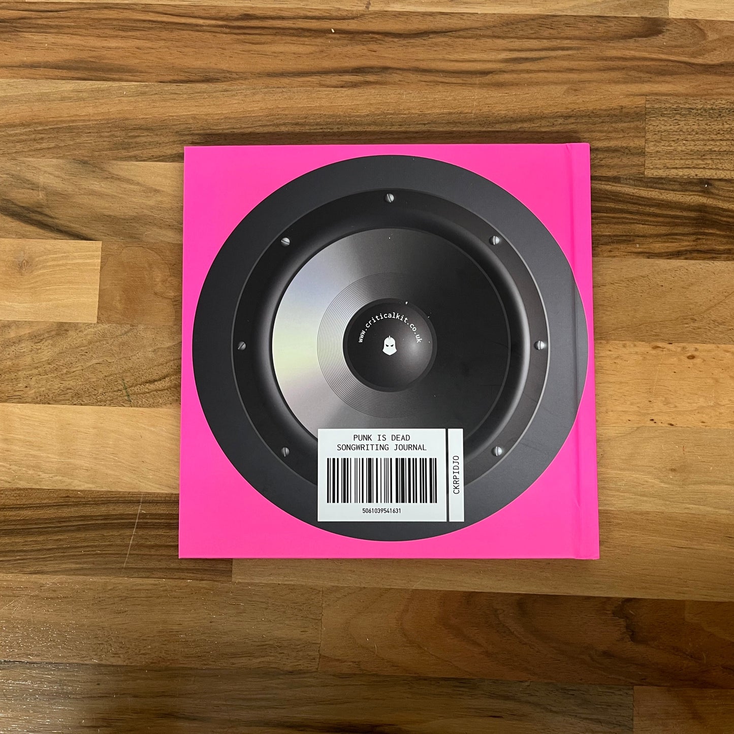 Black speaker on a pink card with a barcode, placed on a wooden surface.