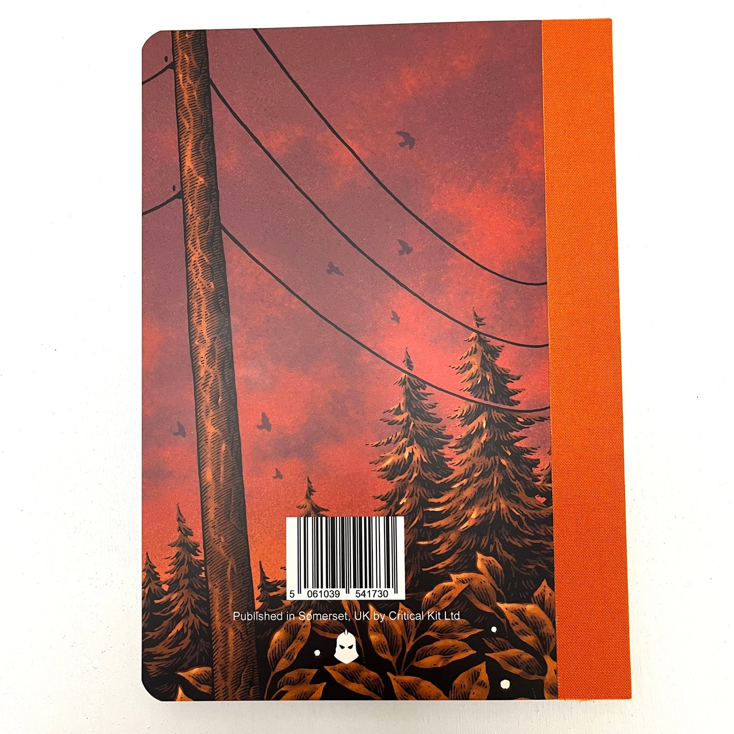 Notebook with orange fabric spine and red and purple sky with douglas fir trees and a telephone pilon.