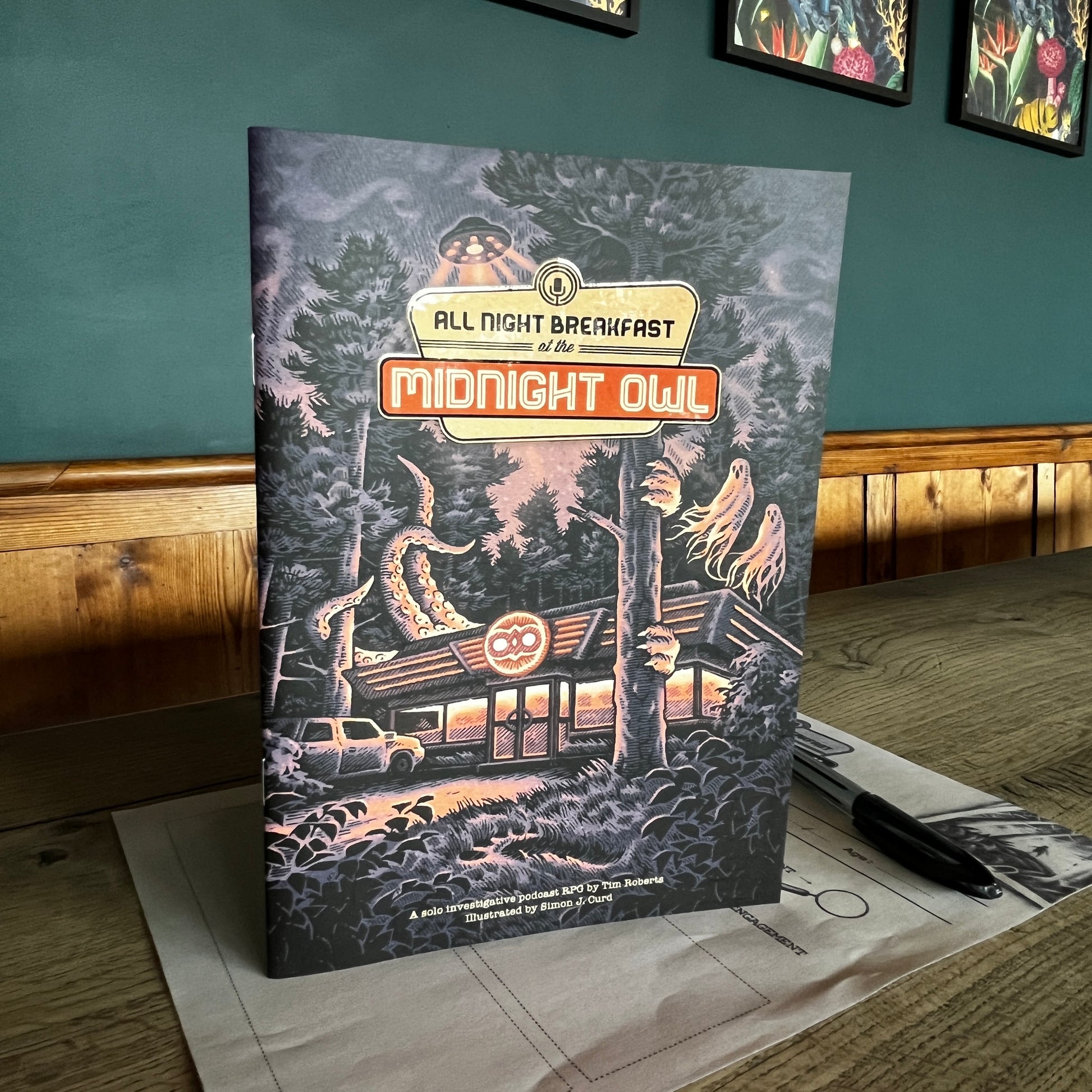 All Night Breakfast a cosy solo role playing game stood up on the character sheet with a pen in a coffee shop with a teal back ground