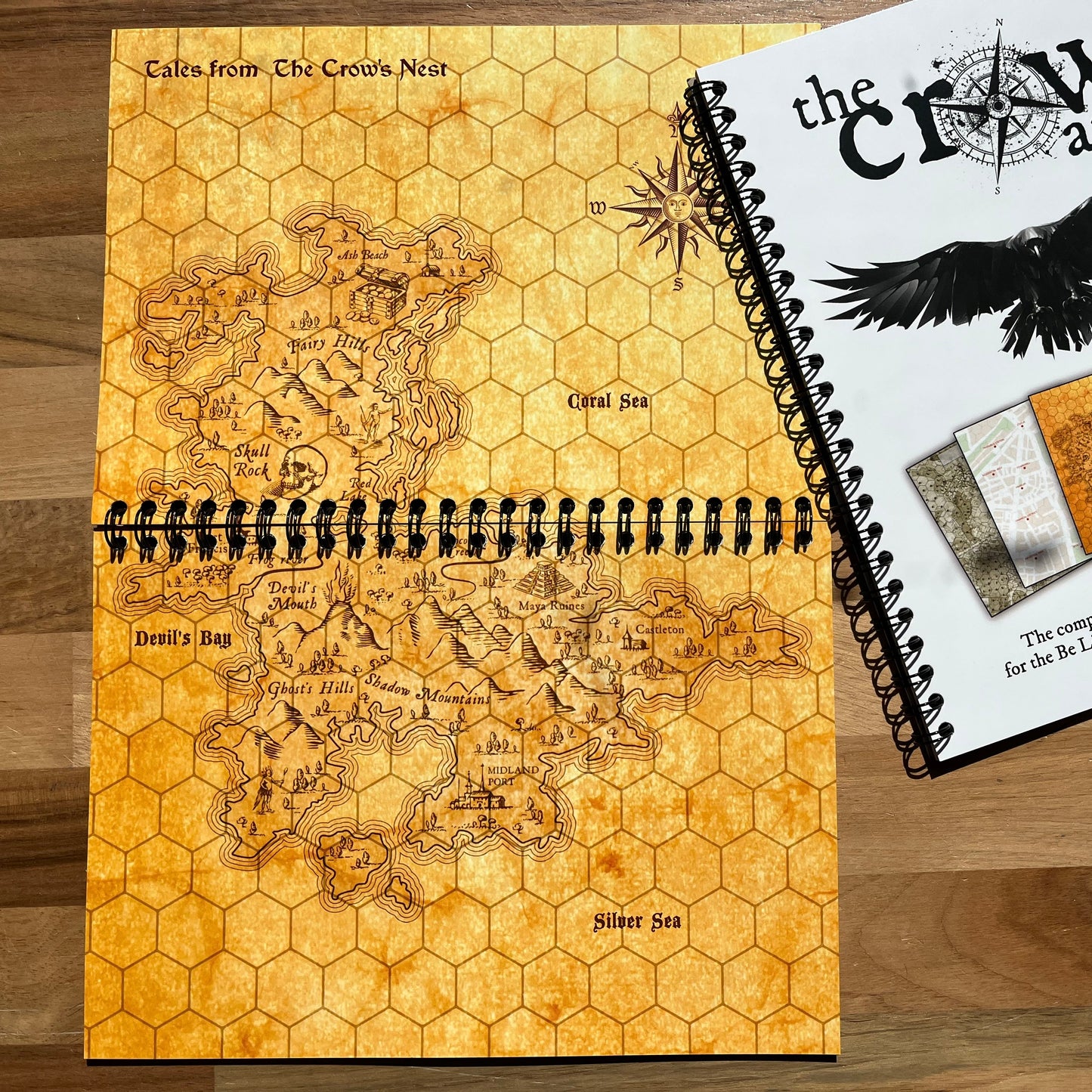 Map book with hexagonal grid design and 'The Crow Atlas' cover on a wooden surface