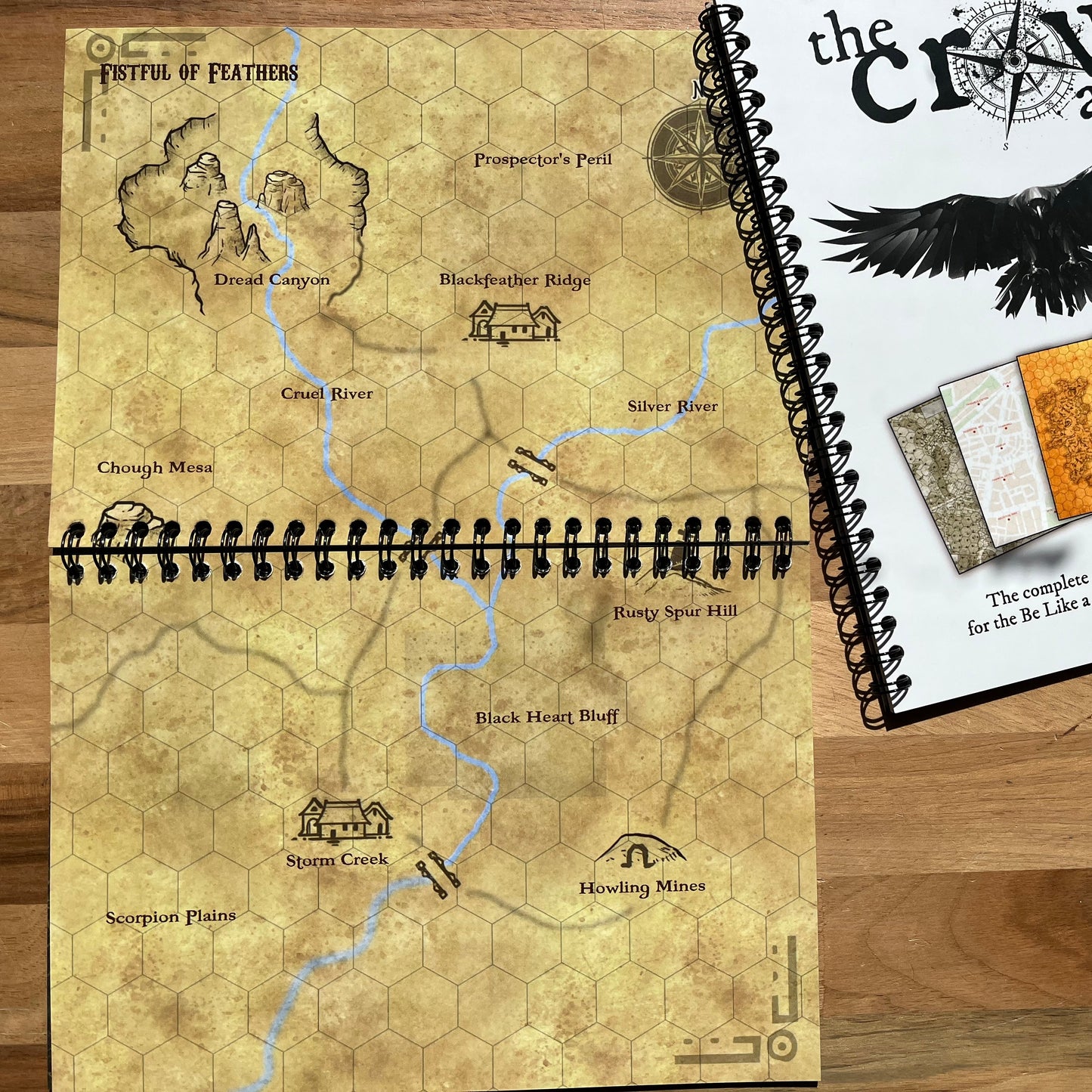 Worn fantasy map book on a wooden surface with 'The Craw Atlas' cover.