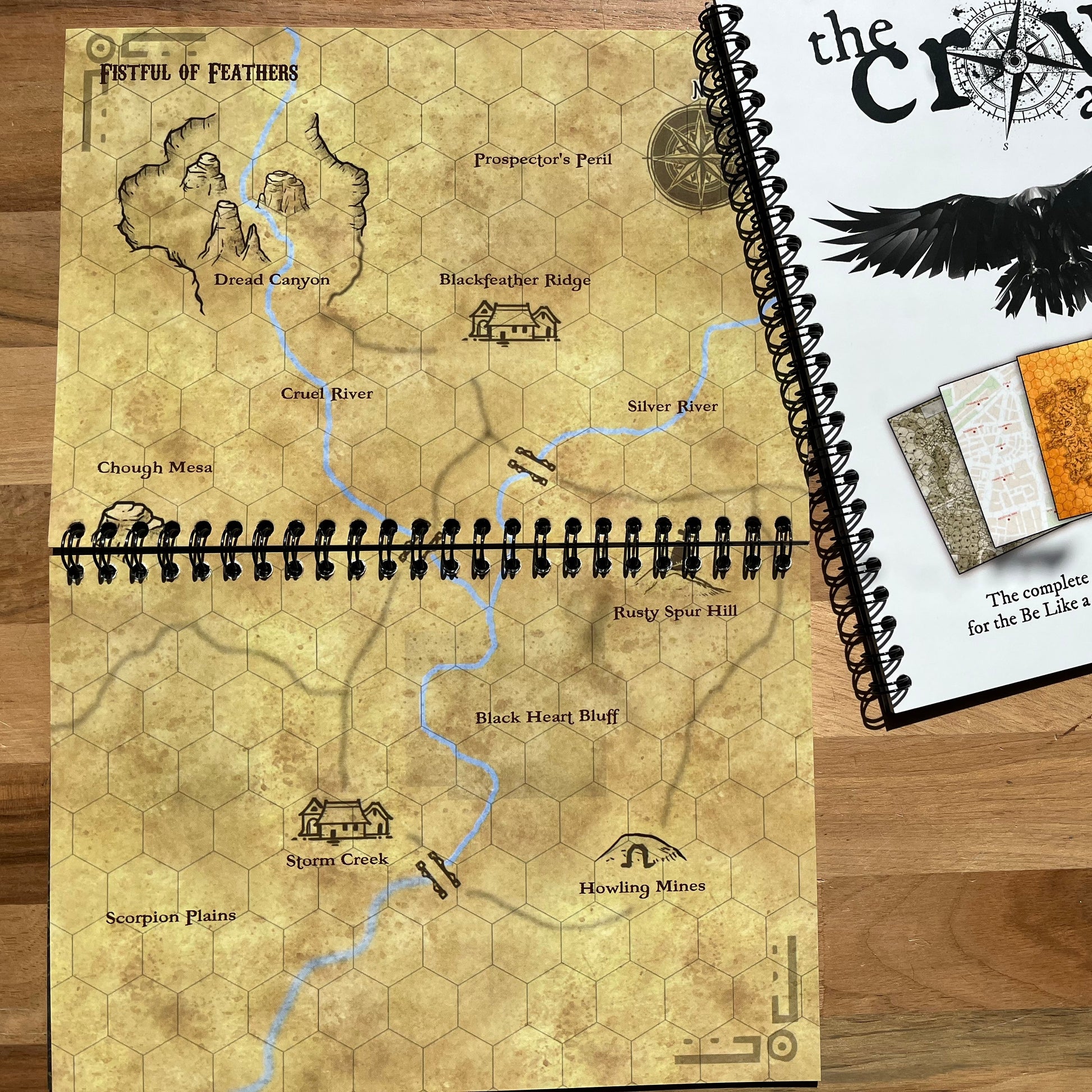Worn fantasy map book on a wooden surface with 'The Craw Atlas' cover.