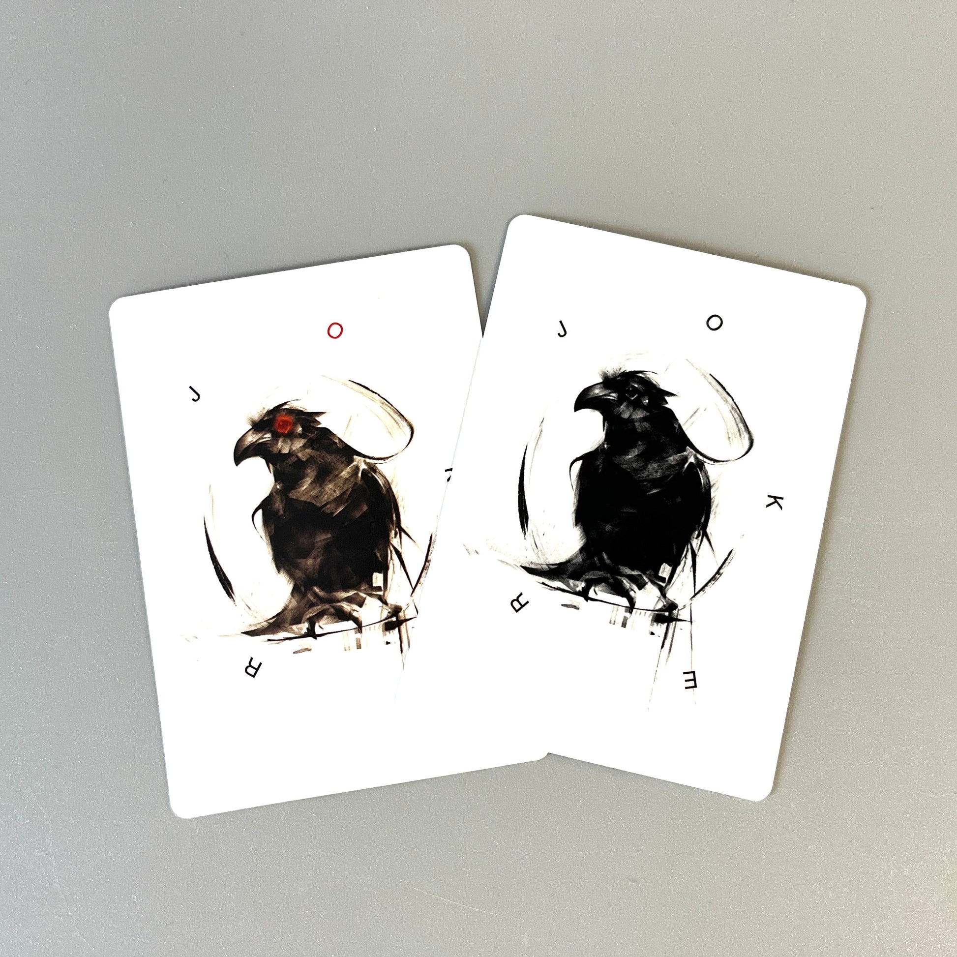 Two white cards featuring black ink illustrations of ravens, displayed on a neutral gray background.