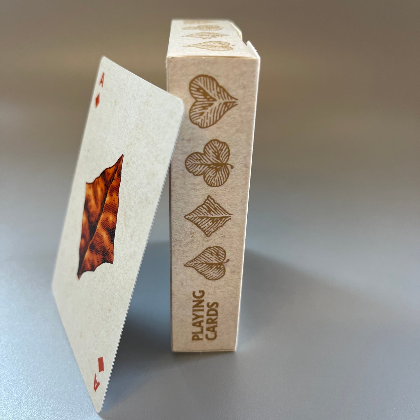A deck of wires in the woods playing cards showing the box spine with the suits illustrated as leaves and the Ace card leaning against the box
