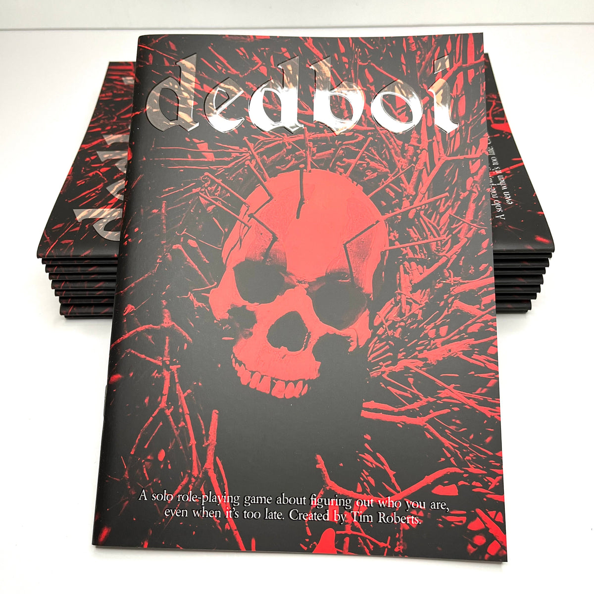 A stack of 'dedboi' solo role playing investigation game boxes on a white surface, with the front box showing a black cover featuring a red skull and red splatter design.