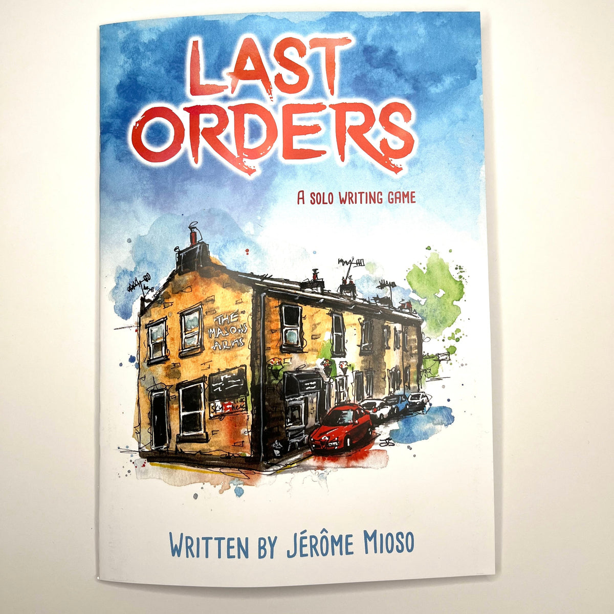 A book or game cover titled "Last Orders" with a watercolor illustration of a row of a pub and a red car, photographed against a plain light background.