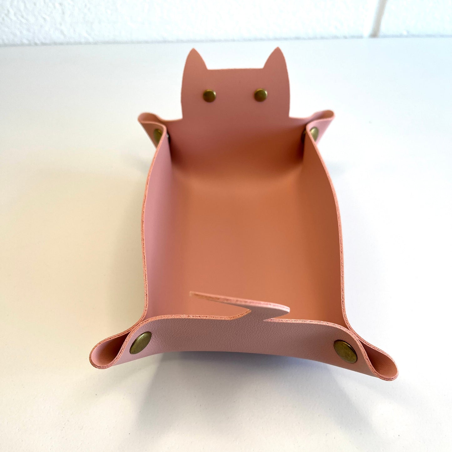A pink cat-shaped dice tray with small gold-tone metal eye and ear accents, photographed on a plain white surface.