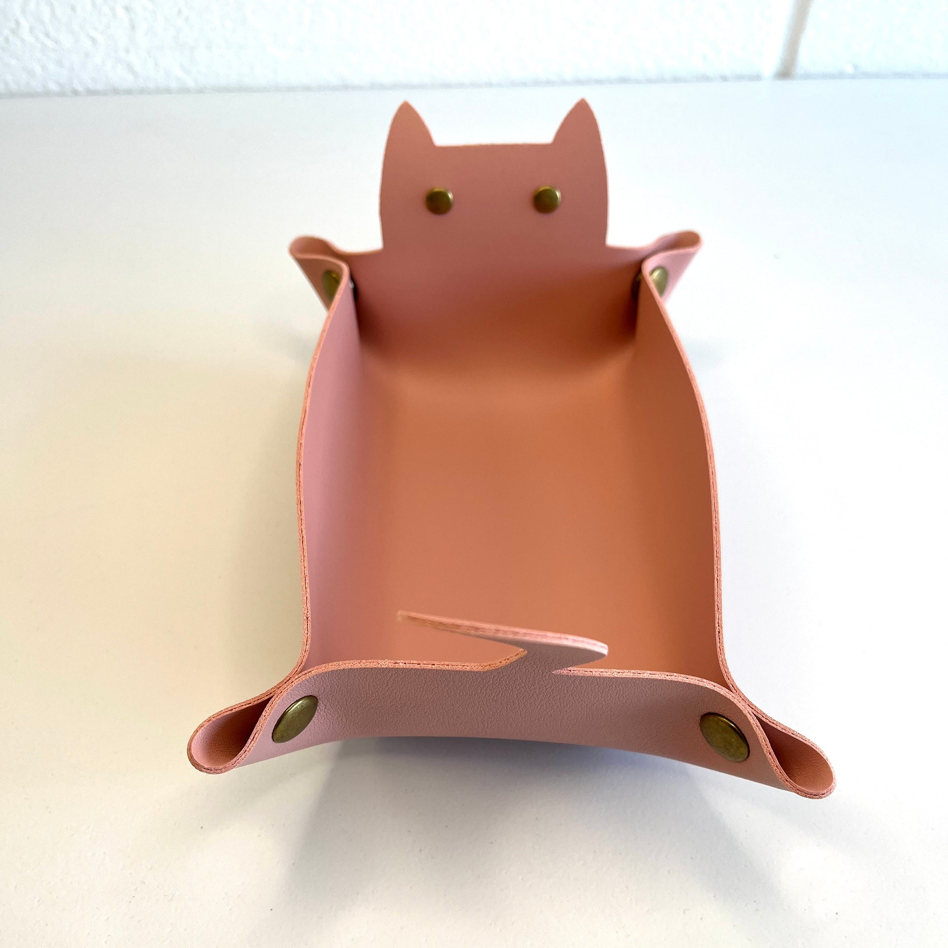 A pink cat-shaped dice tray with small gold-tone metal eye and ear accents, photographed on a plain white surface.